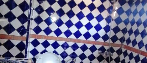 Un baño con pared de baldosas a cuadros, inodoro blanco y suelo de baldosas con diseño geométrico.