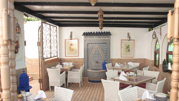 Un área de comedor al aire libre con mesas y sillas de mimbre blanco, baldosas de suelo estampadas y faroles decorativos.