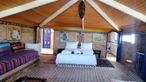 Una habitación con techo de madera alta, una cama con ropa blanca, un sofá colorido y un armario azul.