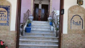Entrada de un hotel con una escalera que lleva a una puerta, un letrero para el restaurante 'Pasta Plaza' y un cartel que dice 'Hotel' en la pared.