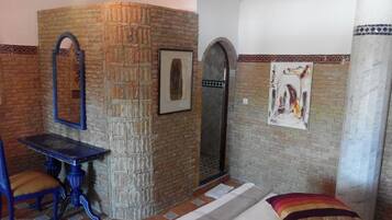 Una habitación con pared de piedra, un cuadro enmarcado, una mesita y una cama con una colcha colorida.