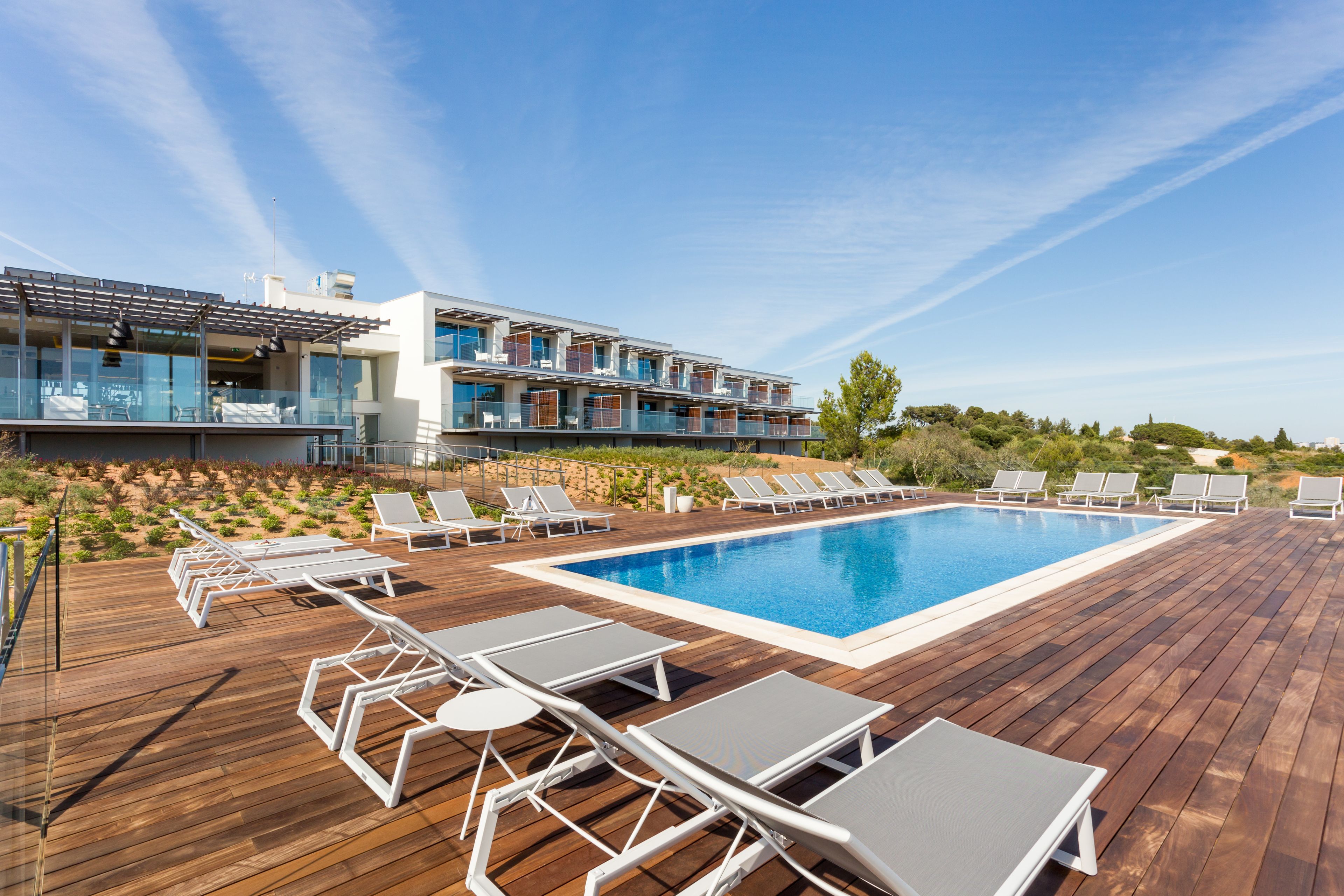 Zona de piscina con tumbonas y un edificio moderno con balcones.