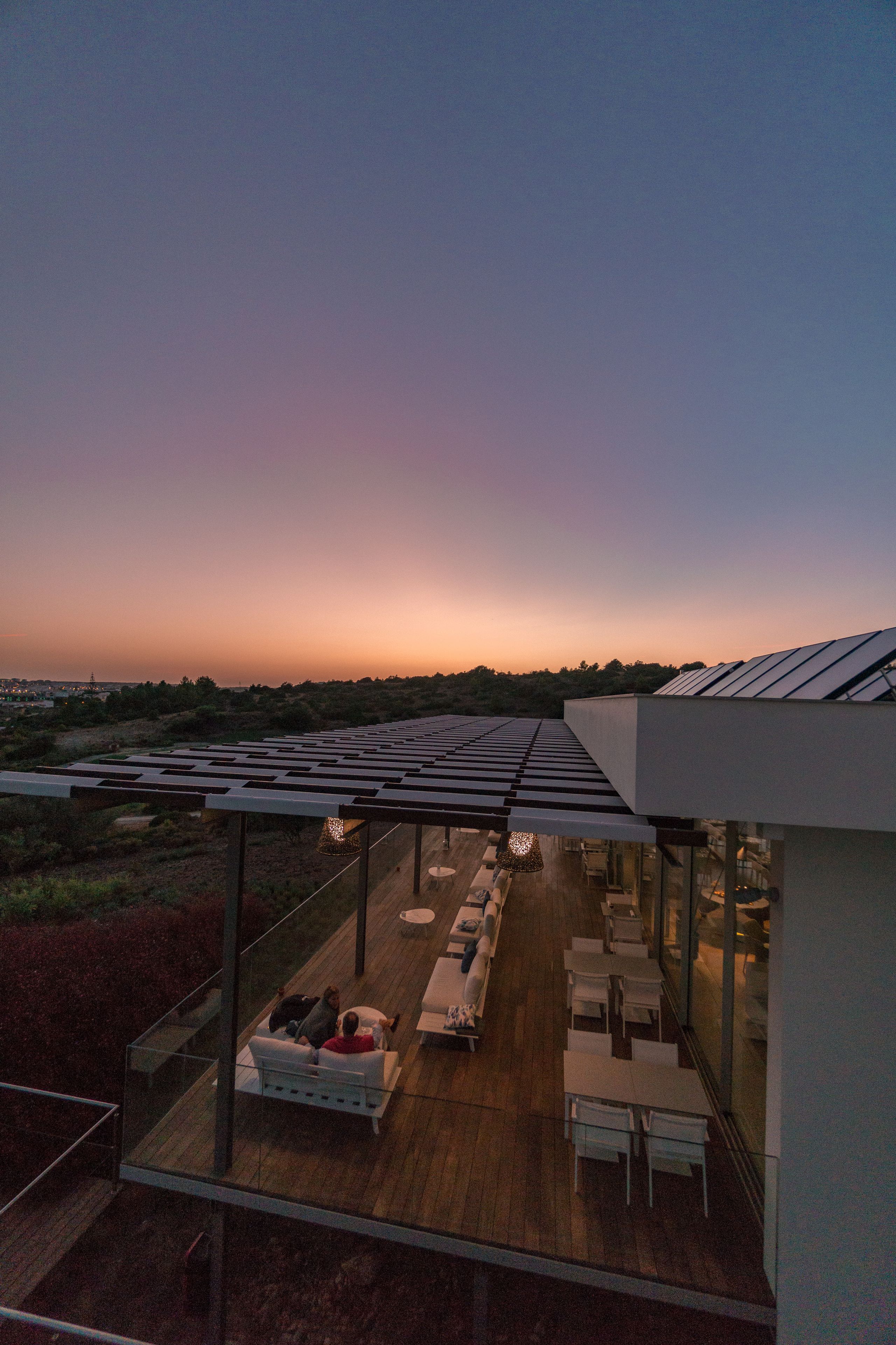 A rooftop terrace with a glass balustrade, outdoor seating, and solar panels.