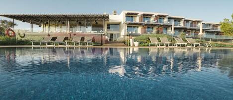 Una piscina al aire libre, sombrillas, sillones reclinables de piscina