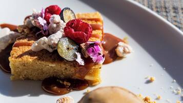 Un plato de postre con una rebanada de pastel coronada con frambuesas, una bola de helado y un chorrito de salsa de chocolate.