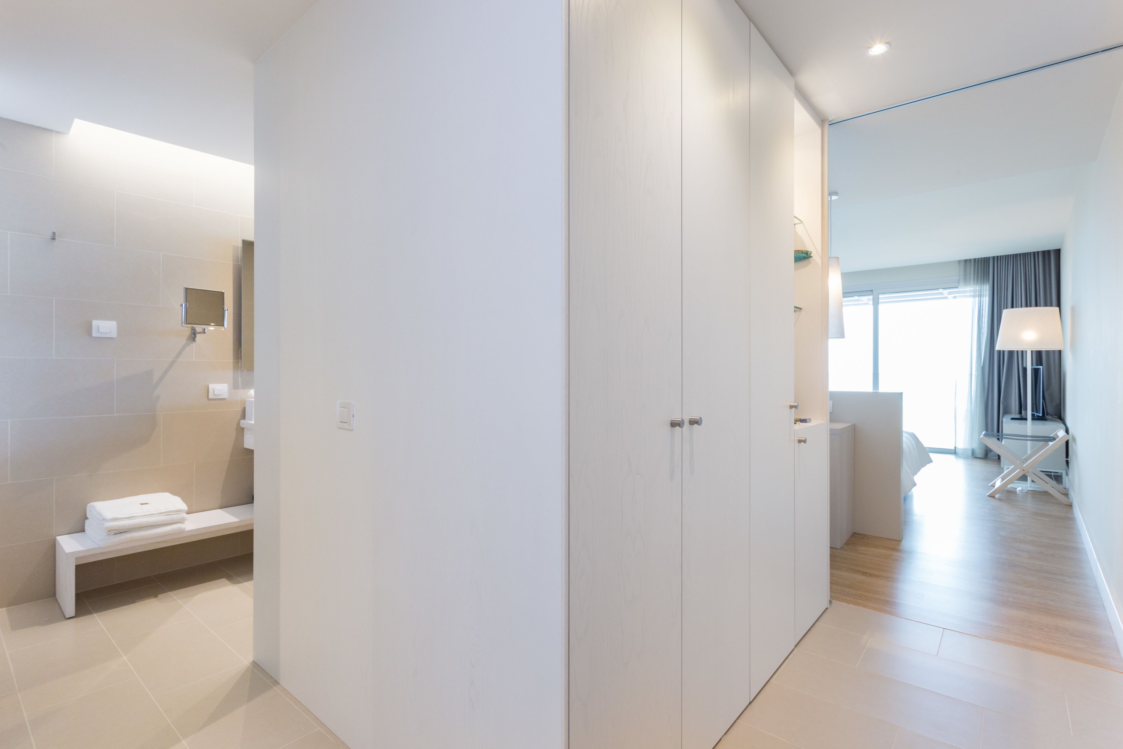Une chambre d’hôtel moderne dotée d’un grand miroir, d’un banc avec des serviettes et offrant une vue sur la ville grâce à de grandes fenêtres.