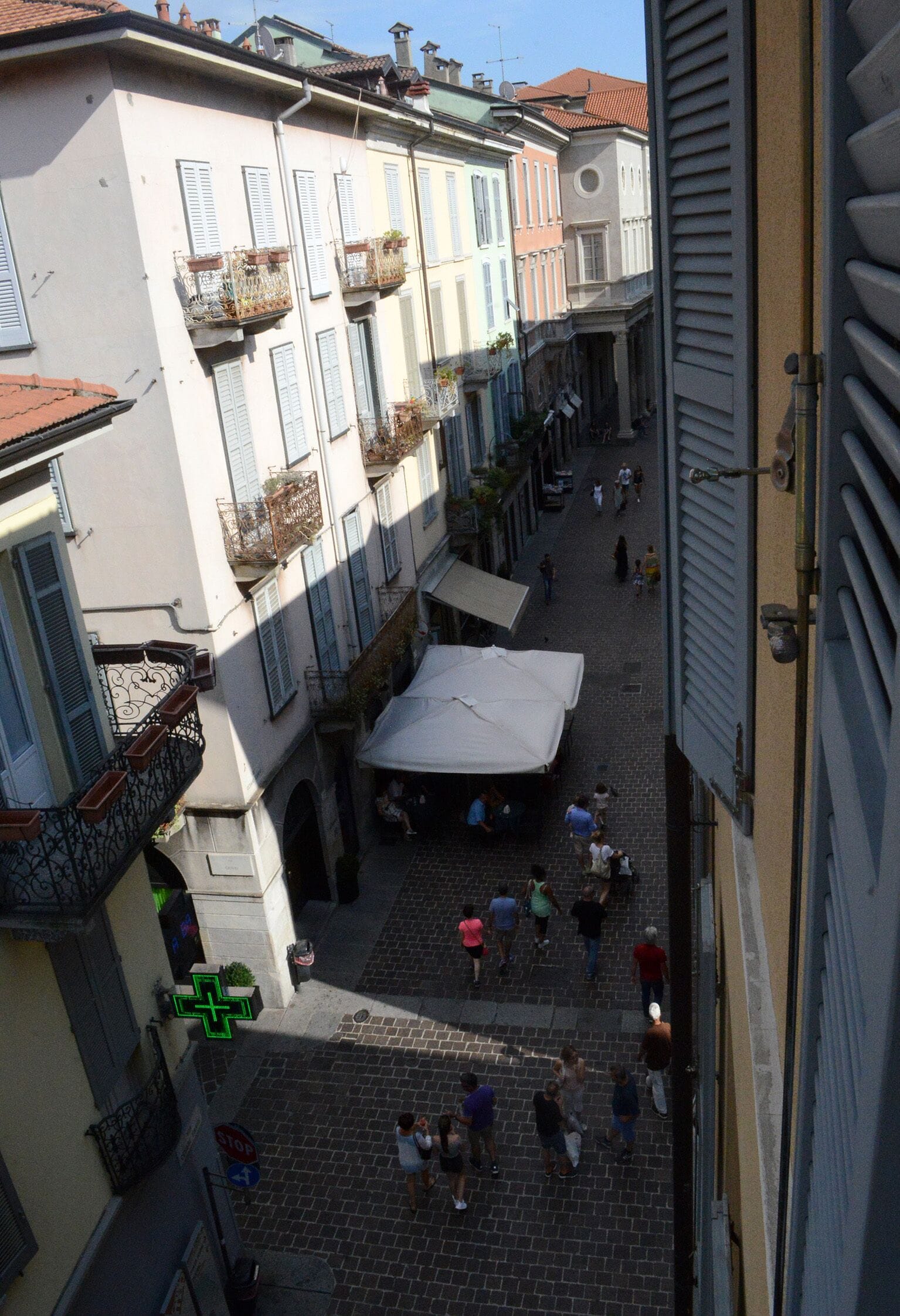 Una calle estrecha flanqueada por edificios con balcones adornados con plantas, y un espacio abierto en el centro con una carpa.