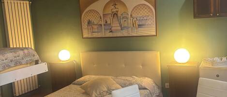 Un dormitorio con cama, mesitas de noche con lámparas, un cuadro en la pared y una pequeña mesa con un vaso.