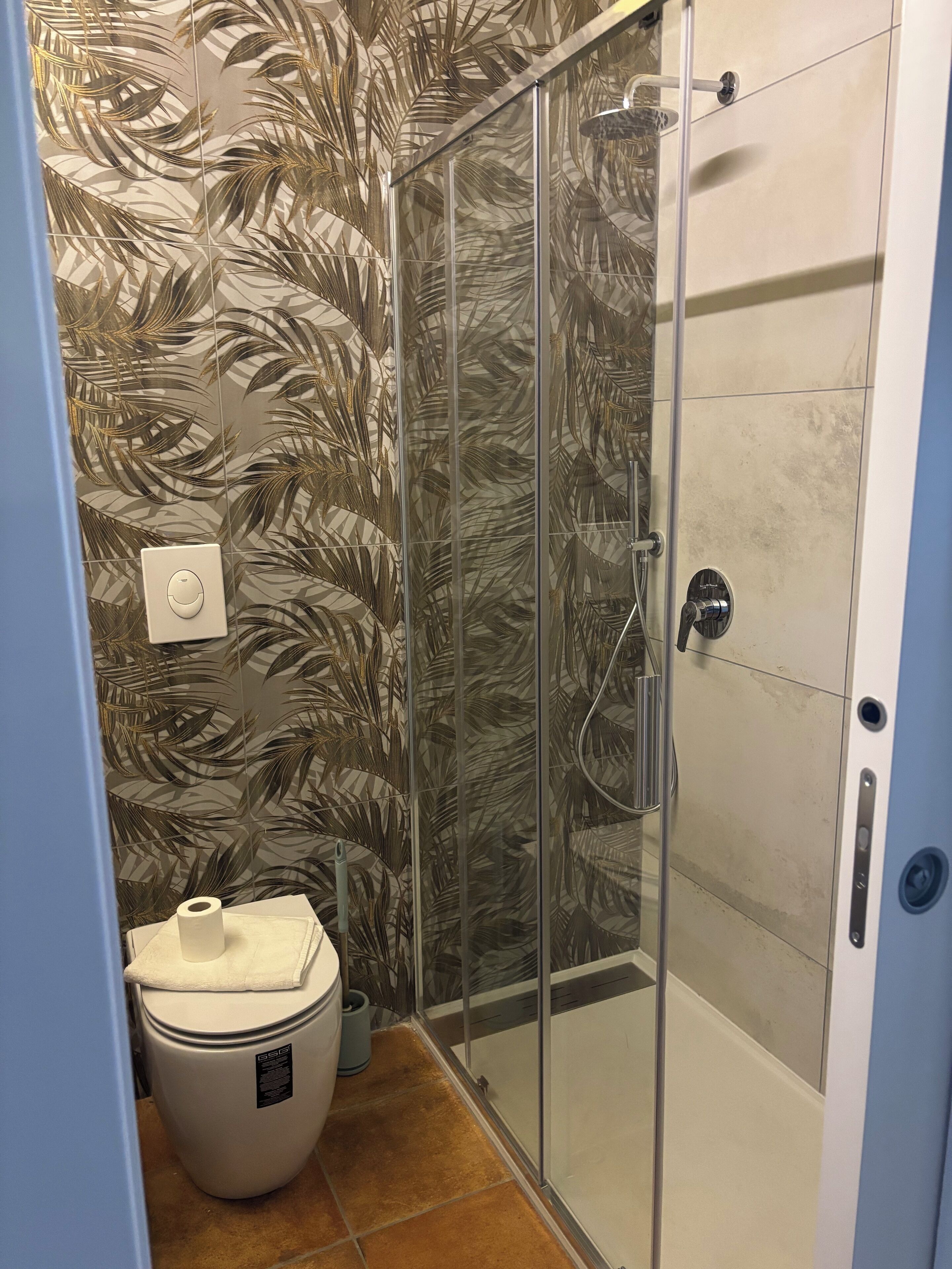 Une salle de bain avec une douche à parois de verre, des toilettes et un mur orné d’un motif de feuilles.