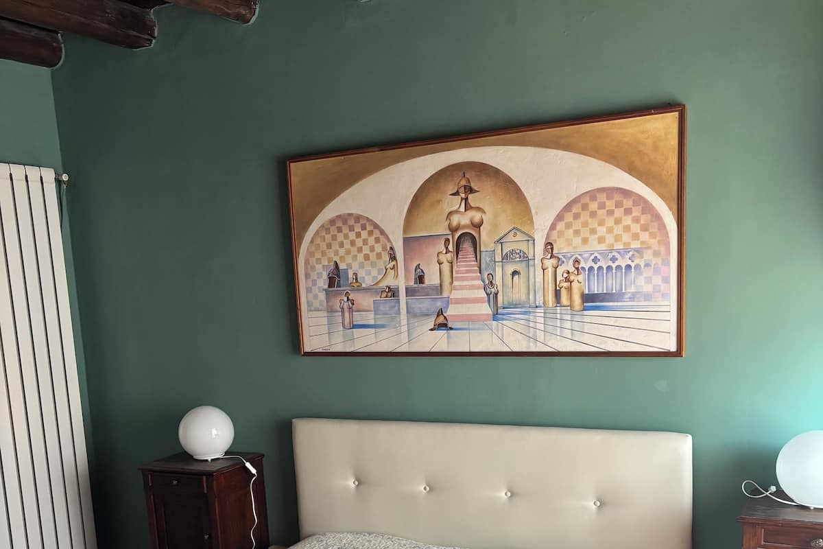 A bedroom with a bed, a painting, a radiator, and a wooden cabinet.