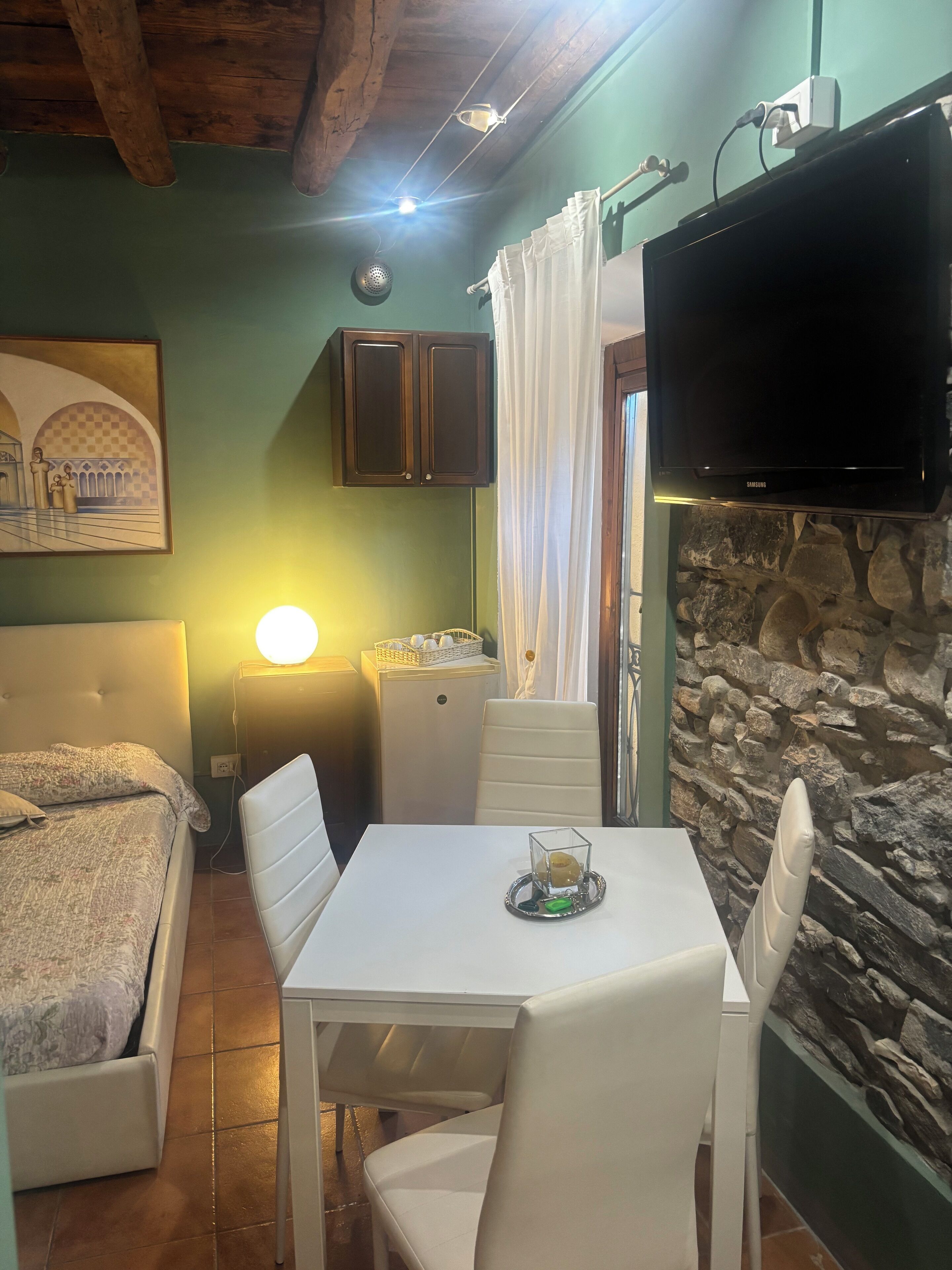 Una habitación acogedora con cama, una mesa con sillas, televisión y una pared de piedra.