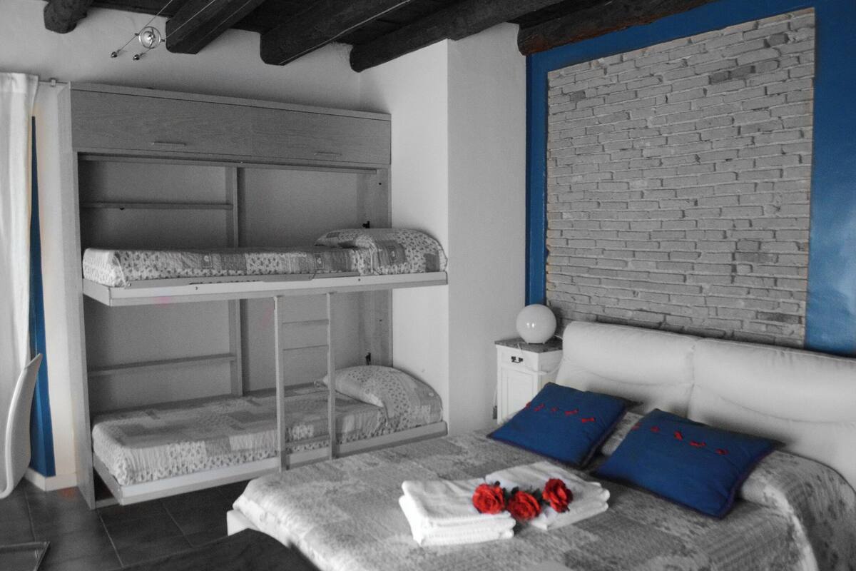 A room with a bunk bed, a bedside table with a lamp, and a brick-patterned wall.