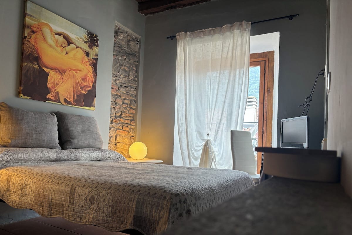 A bedroom with a bed, a nightstand, a lamp, a TV, and a painting on the wall.
