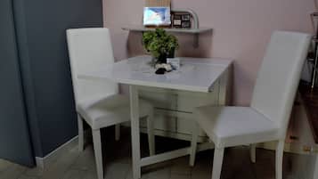 A white dining table with two chairs, a small potted plant, and a shelf with a picture and some items.
