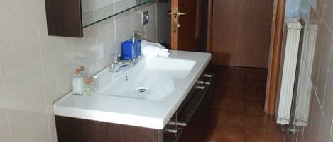 A bathroom with a double sink, a mirror, a toilet, and a shower.