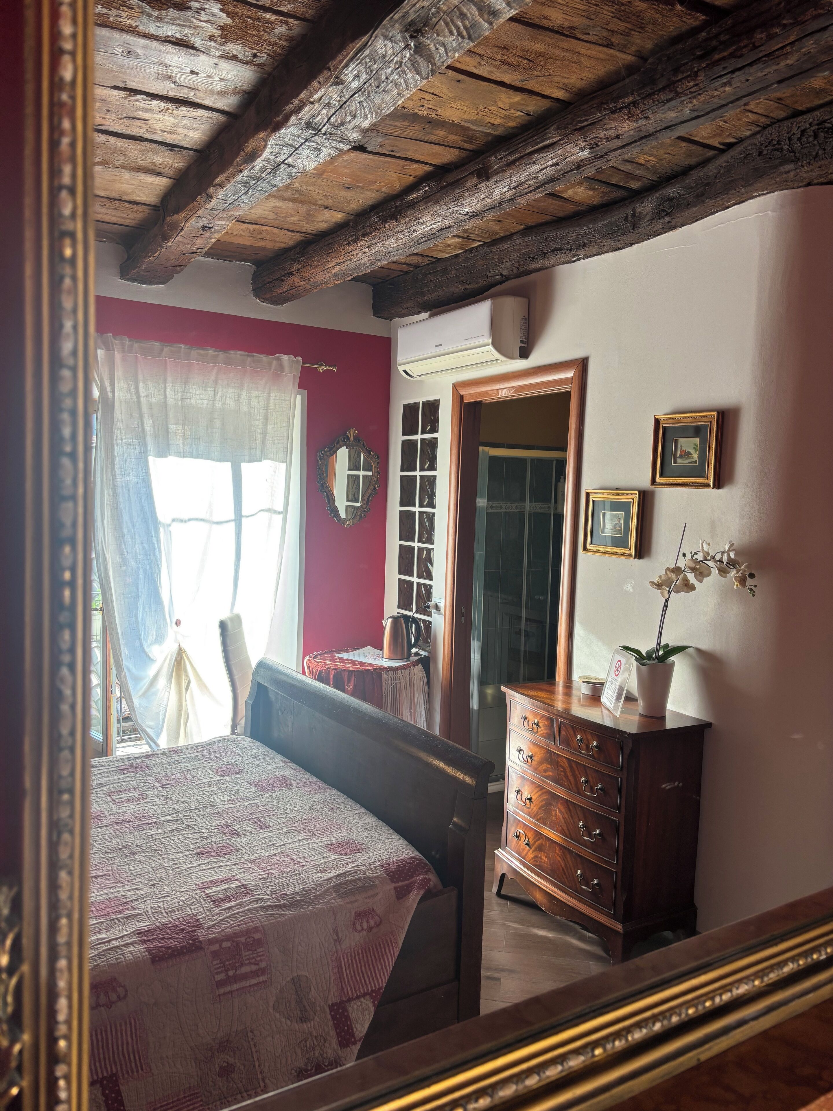 Un dormitorio con techo de madera, una cama con colcha estampada, un aparador y un espejo.