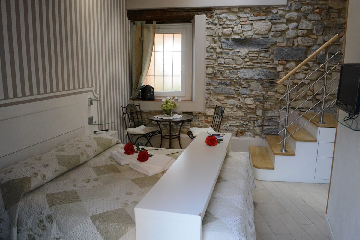 A cozy room with a stone wall, a wooden staircase, a white bench, and a small table with a vase of flowers.