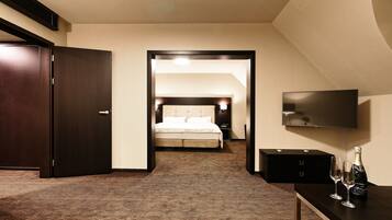 A hotel room with a bed, a TV, a minibar, and a bottle of champagne.