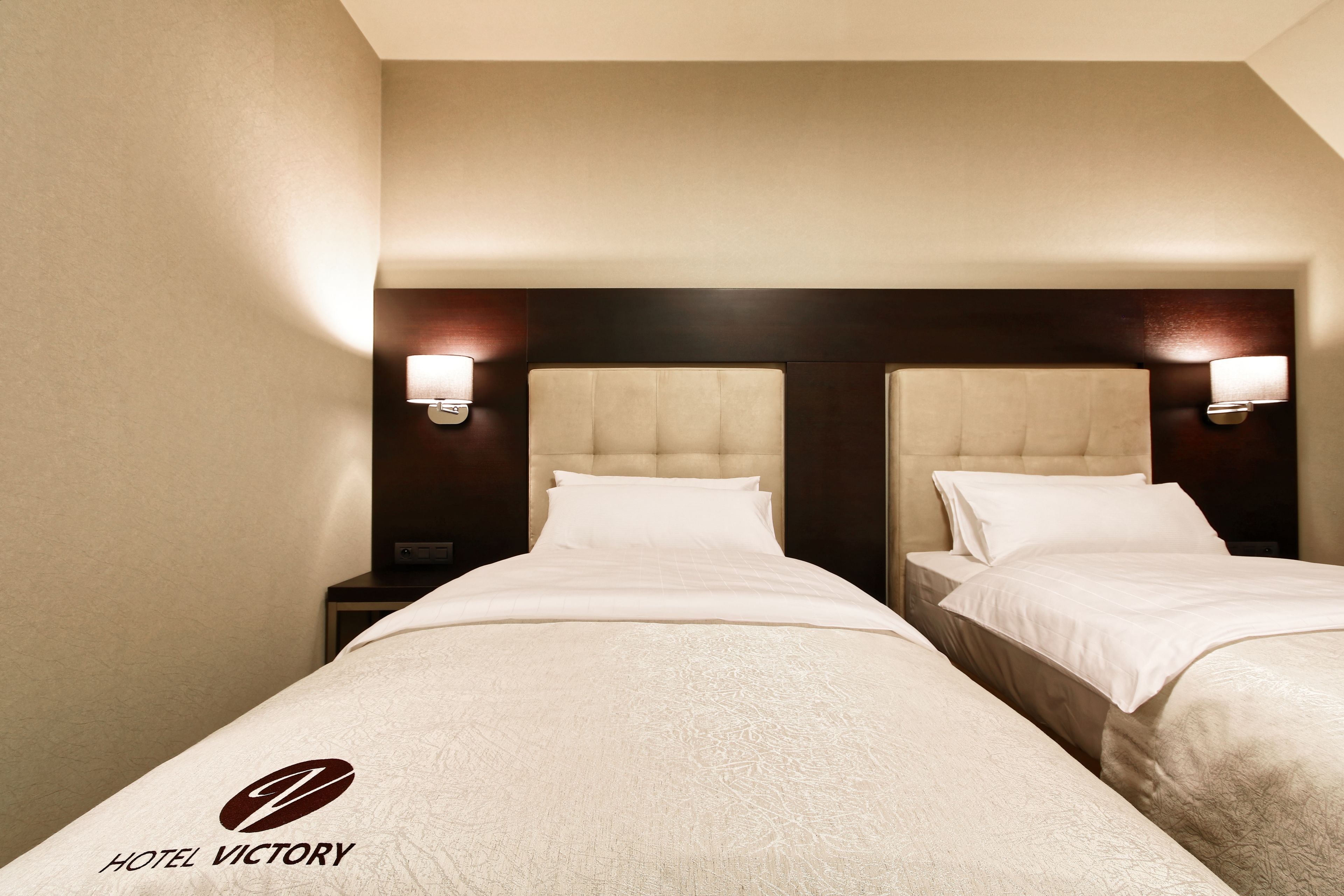 Habitación de hotel con dos camas, cada una con cabecera y lámparas de noche.