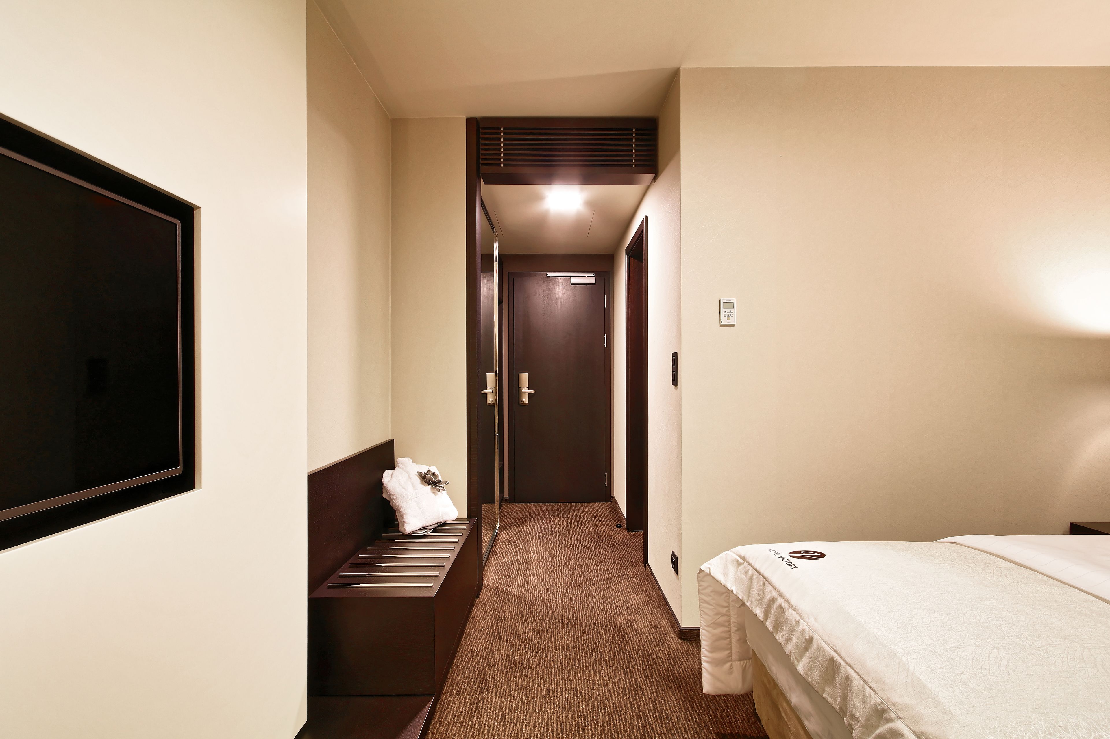 A hotel room with a bed, a bench with a towel, a mirror, and a door leading to another room.