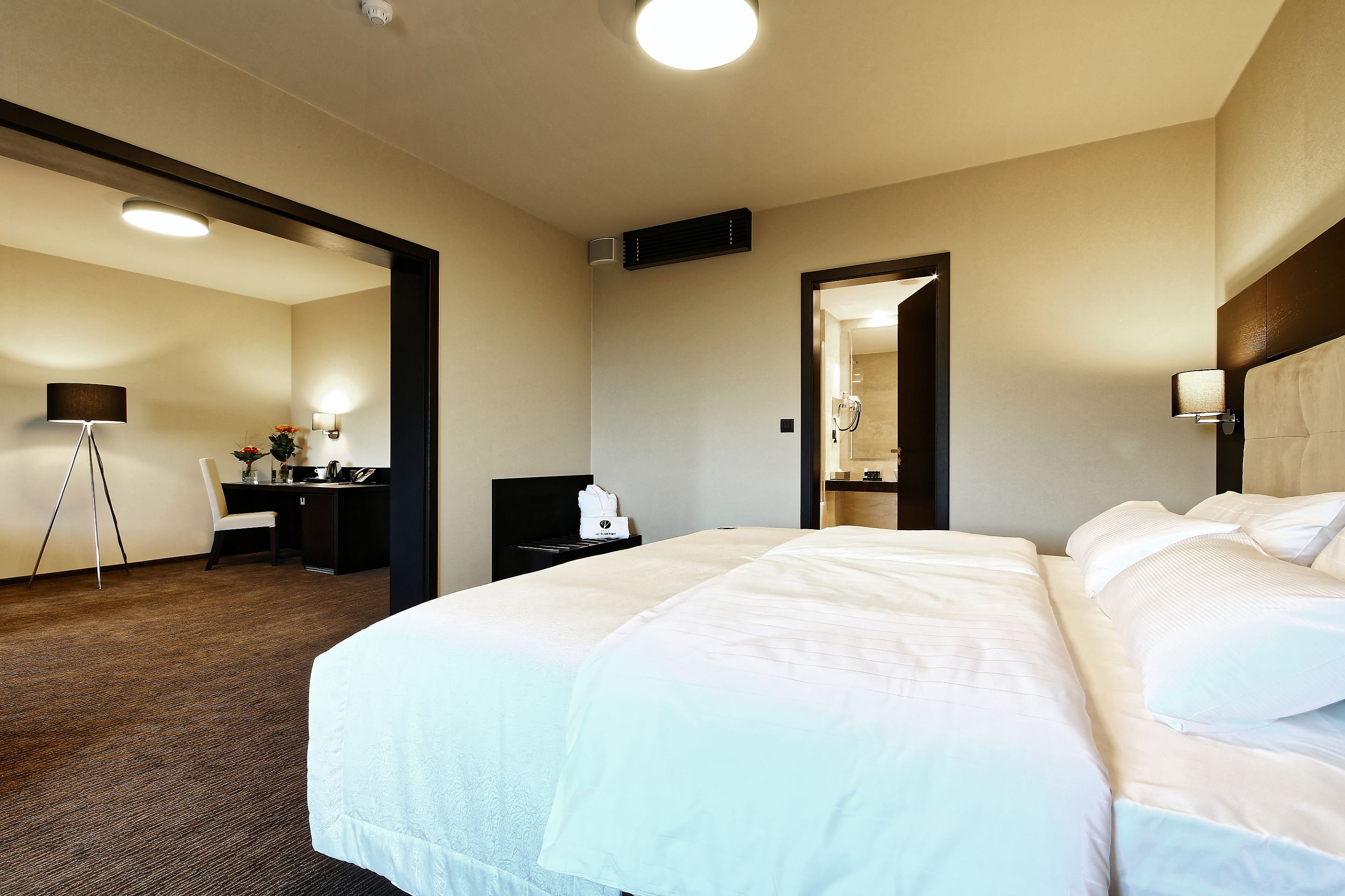 Quarto de hotel com uma cama grande, uma escrivaninha com cadeira, uma luminária e um espelho.