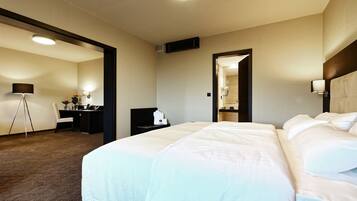 Quarto de hotel com uma cama grande, uma escrivaninha com cadeira, uma luminária e um espelho.