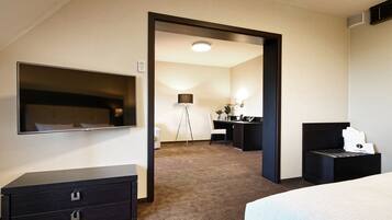 A hotel room with a bed, a dresser, a desk, a chair, and a television on the wall.