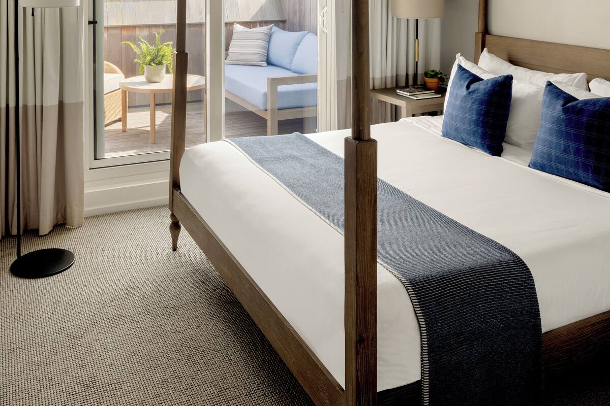 Habitación de hotel con una cama grande, un balcón con vistas y una pequeña mesa con una silla.