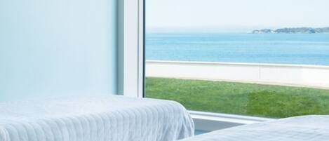 A bedroom with two beds, a large window, and a view of the sea.