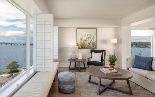 A modern living room with a view of a bridge over water, a sofa, a chair, a coffee table, and a side table with a lamp and decorative items.