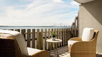 Ein Balkon mit Korbmöbeln, einem kleinen runden Tisch mit einer Pflanze und Blick auf eine Brücke über dem Wasser.