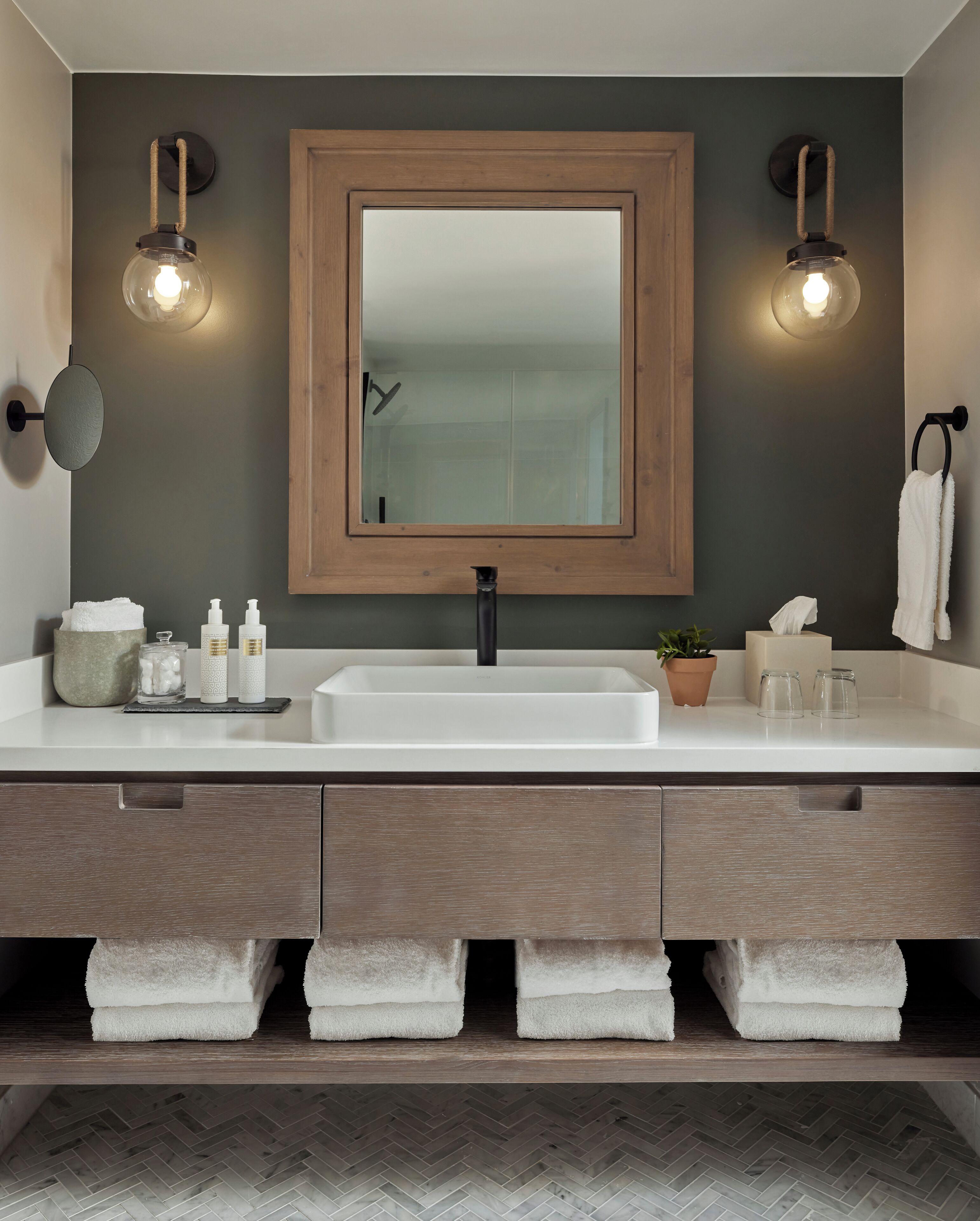 A modern bathroom with a large mirror, two wall-mounted lights, a sink, and a towel rack.