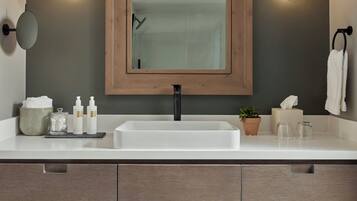 A modern bathroom with a large mirror, two wall-mounted lights, a sink, and a towel rack.