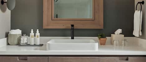 Un baño moderno con un espejo grande, dos luces en la pared, un lavamanos y un perchero para toallas.