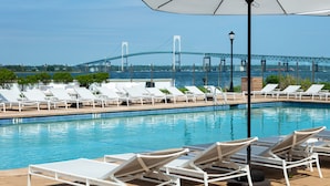 A pool area with lounge chairs and an umbrella, a bridge in the background, and a clear sky. - Newport Harbor Island Resort (Newport)
