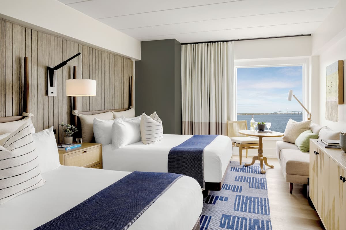 Habitación de hotel con dos camas, un escritorio, una silla, una mesita y vistas al mar.