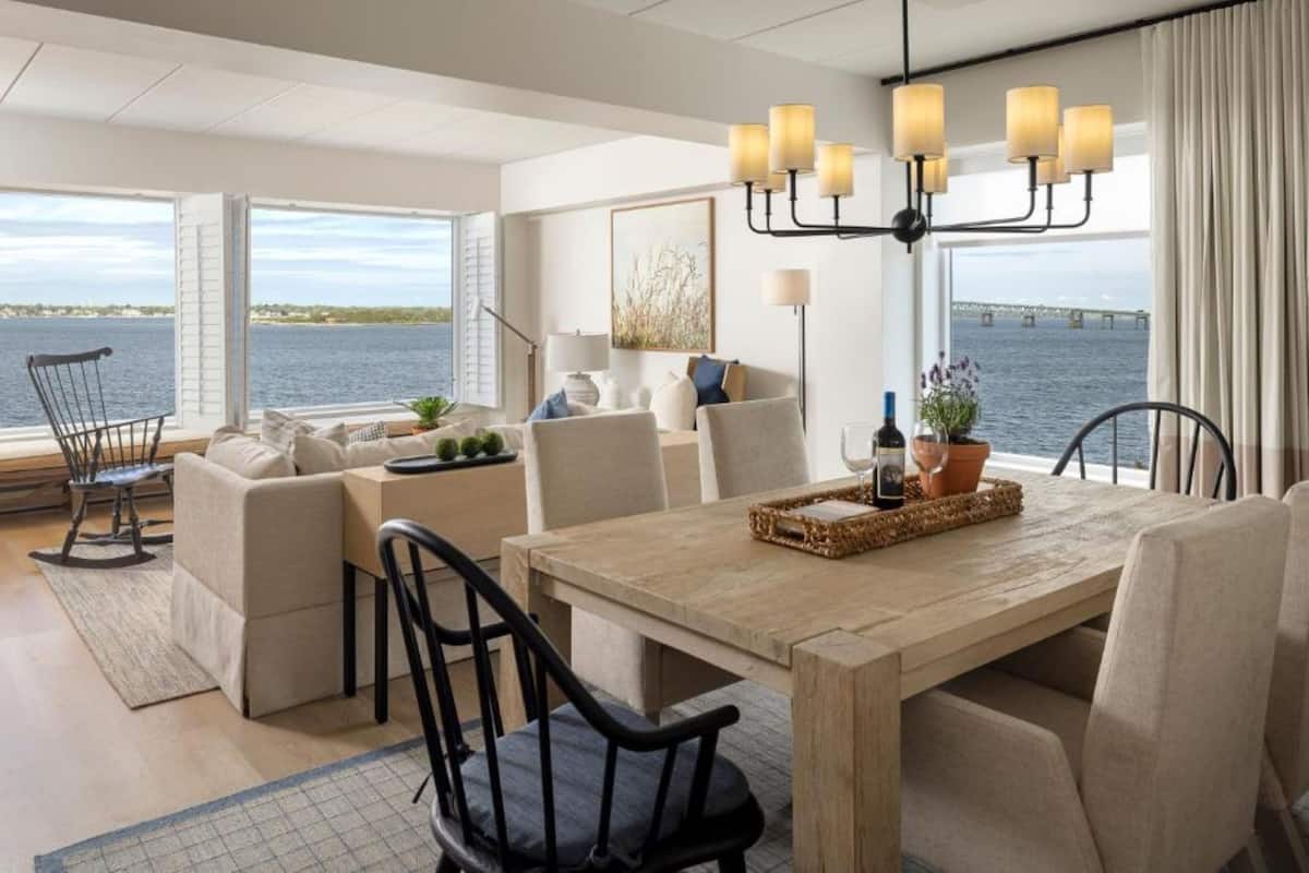 Una sala de estar moderna con vista al agua, una mesa de comedor de madera y un candelabro.