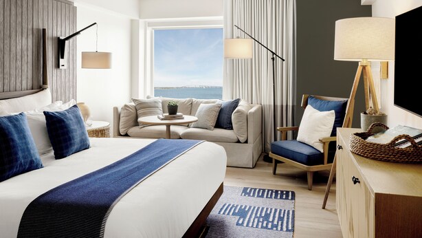 Habitación de hotel con una cama grande, un sofá, una silla, una mesita y un televisor.