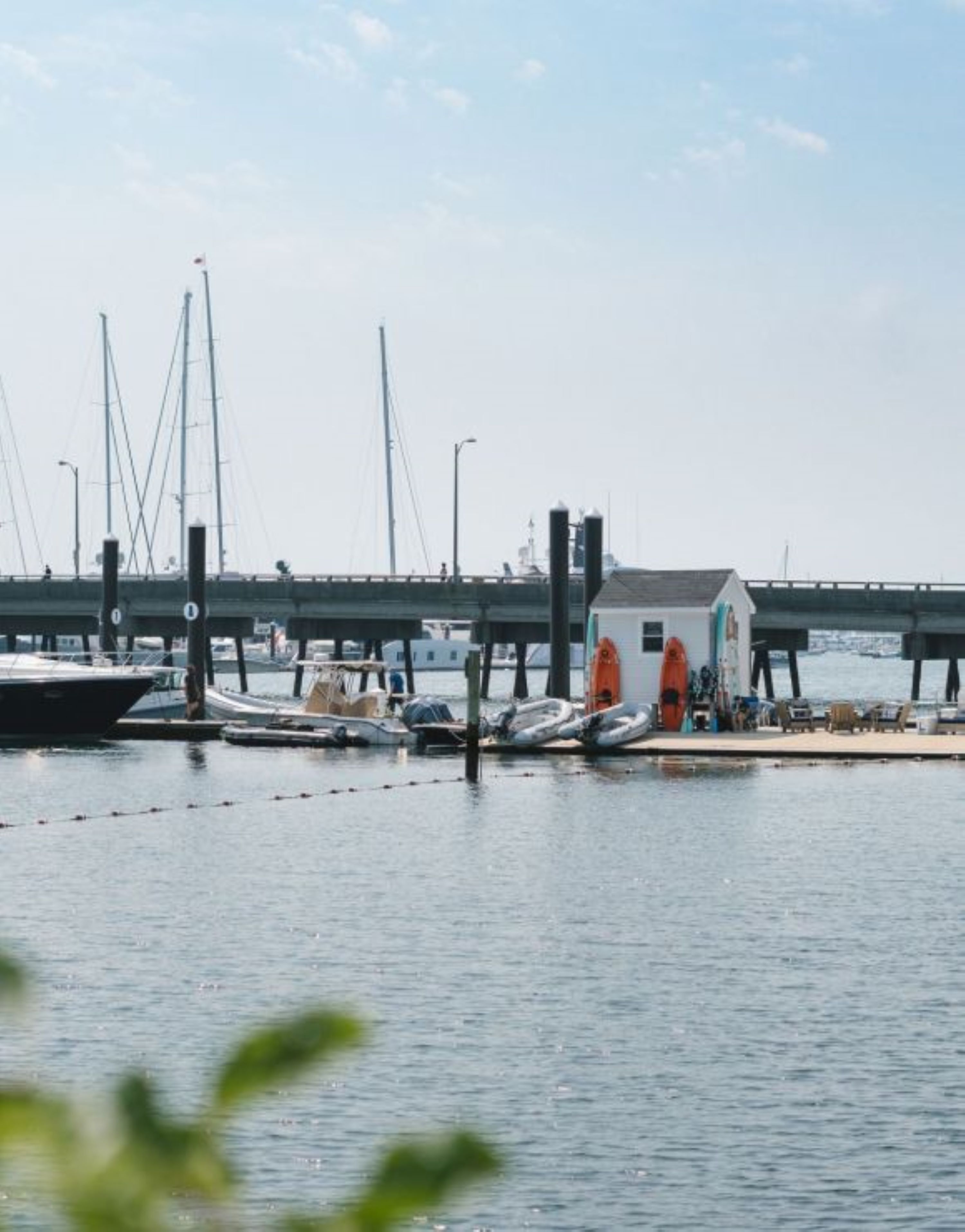 A marina with boats docked, a bridge in the background, and a building with outdoor seating.