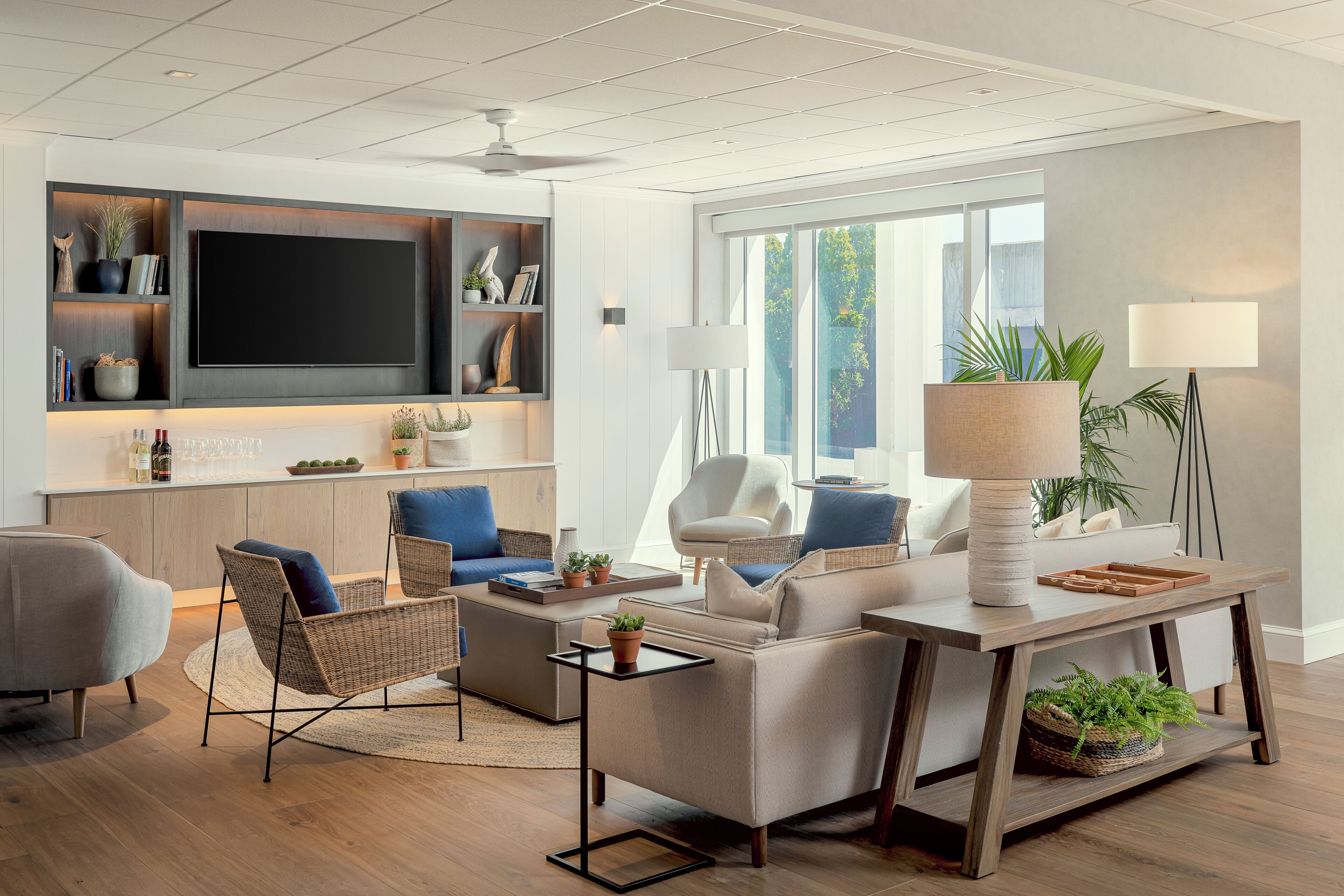 A modern living room with a flat-screen TV, comfortable seating, and a large window providing natural light.