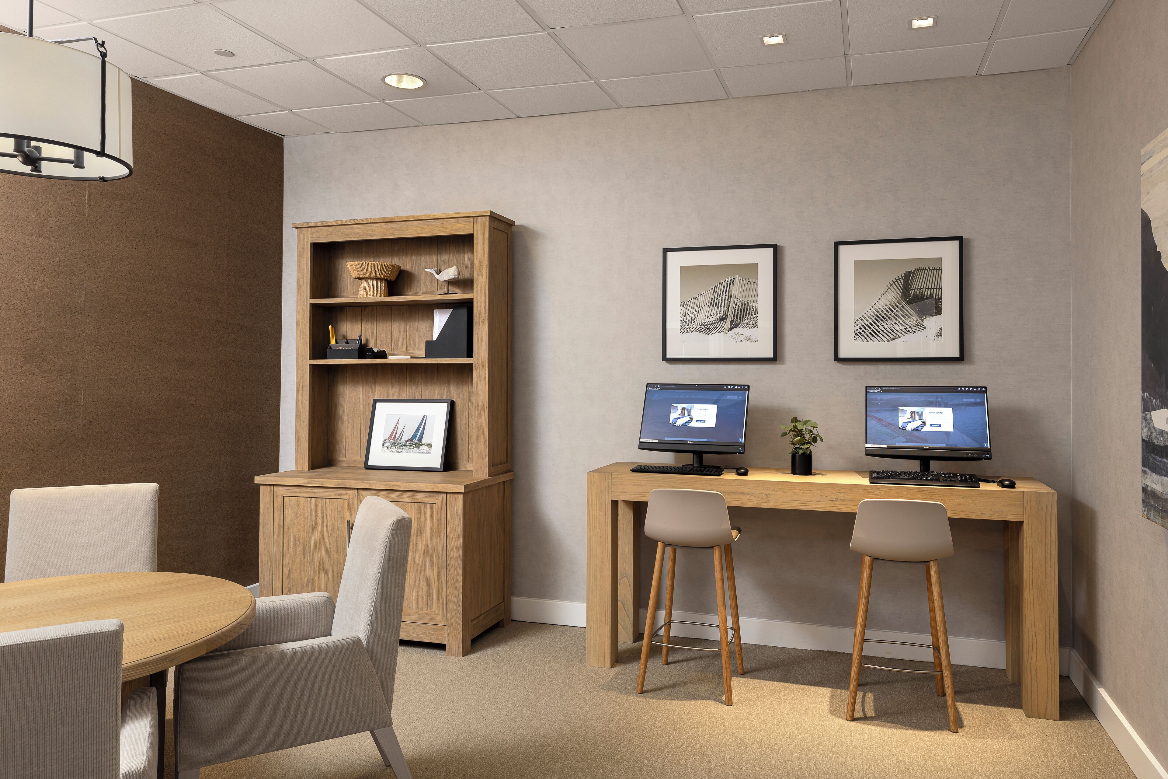 A modern office space with a wooden desk, two computers, a bookshelf, and a round table with chairs.