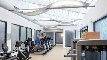 Une salle de sport équipée de tapis de course, de vélos d’appartement et d’une machine à développé couché.