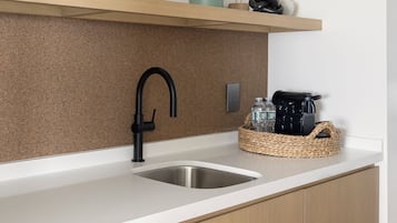 A kitchen with a stainless steel sink, a black faucet, and a woven basket containing water bottles and a coffee maker.