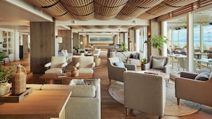 A spacious lounge area with multiple seating options, a wooden ceiling, and large windows offering a view of a bridge and water. - Newport Harbor Island Resort (Newport)