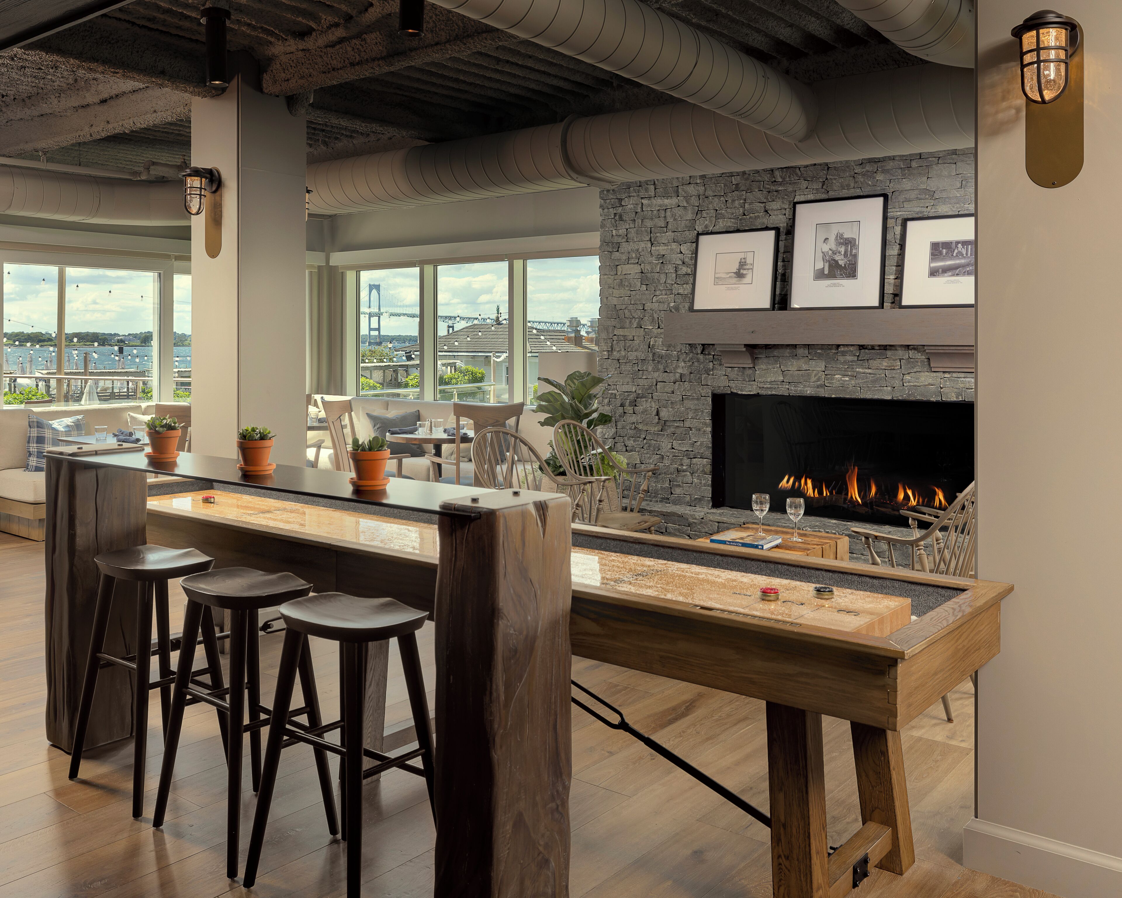 Un área de bar moderna con chimenea de piedra, ventanas amplias y vistas a la ciudad.