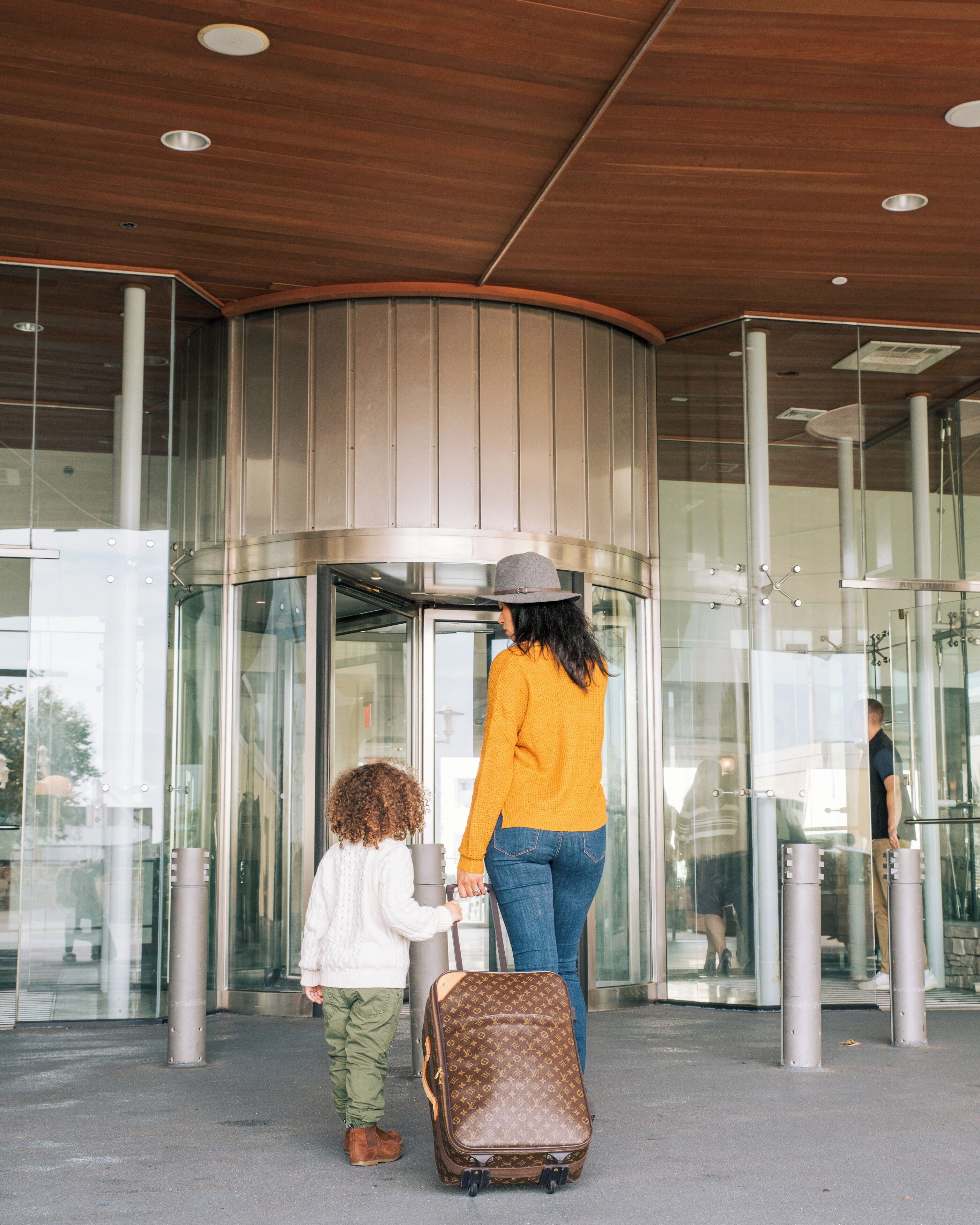 A woman and a child at a revolving door entrance of a building with glass walls and a wooden ceiling.