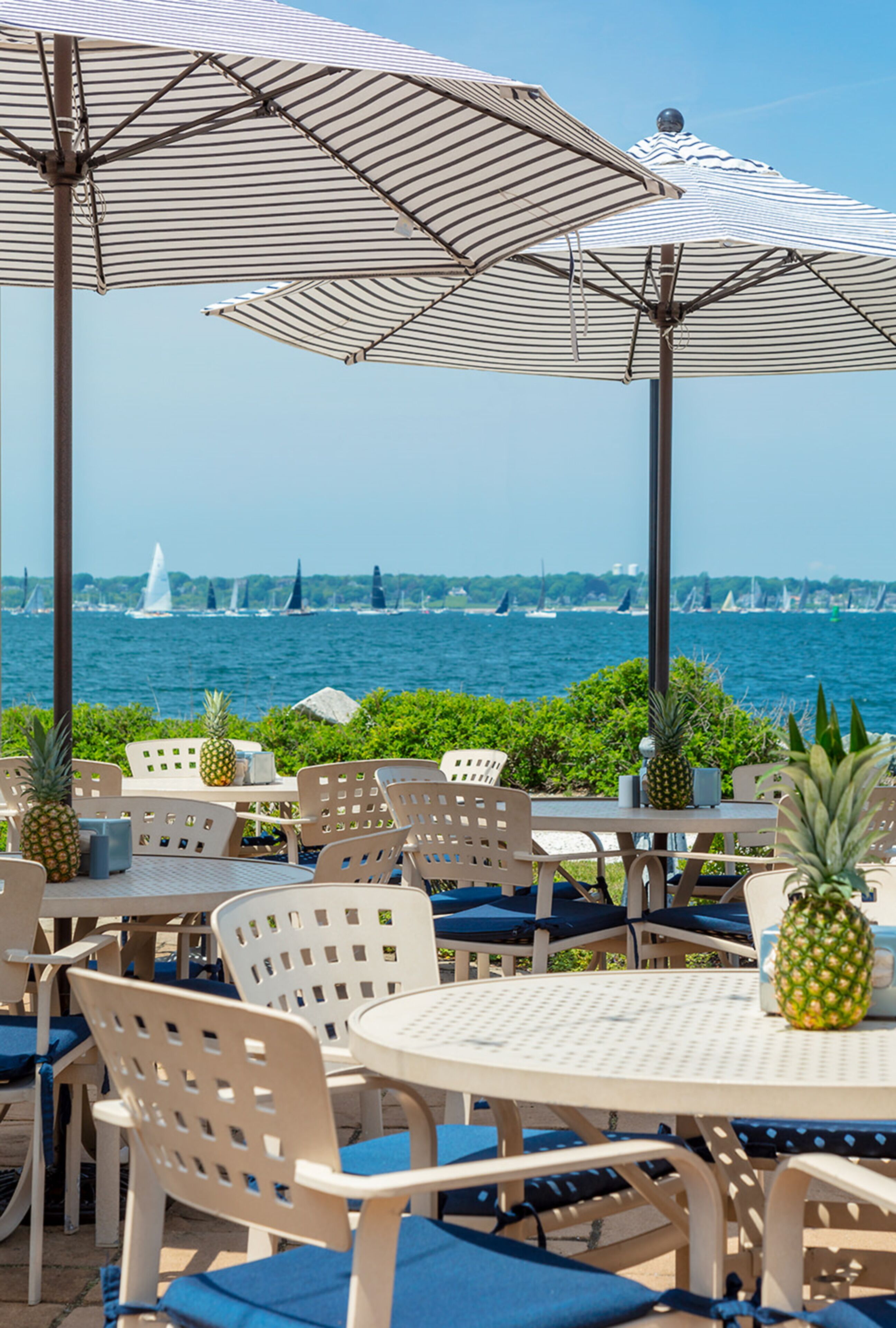 A seaside patio with round tables and chairs, umbrellas, and pineapples.