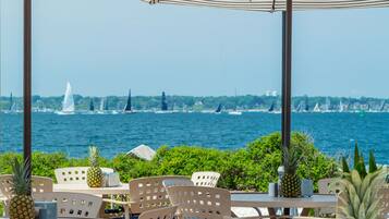 A seaside patio with round tables and chairs, umbrellas, and pineapples.