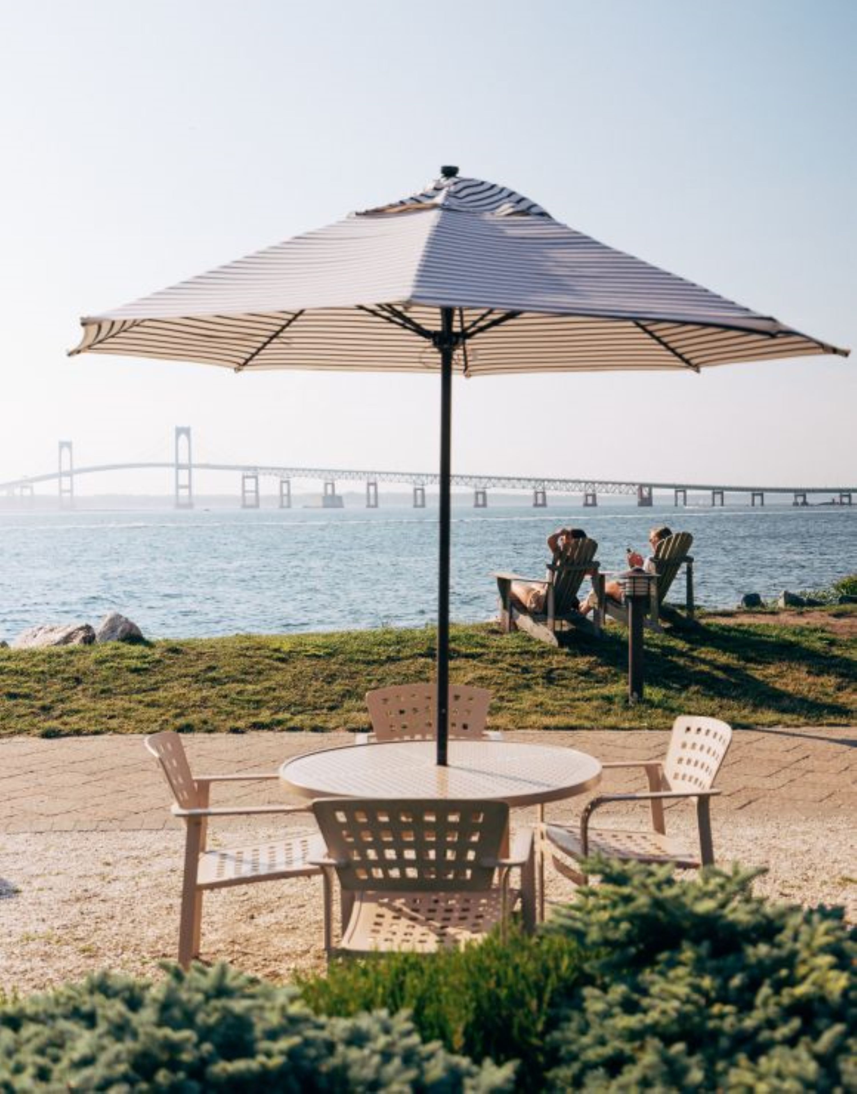 Een terras met een tafel en stoelen, een grote parasol en uitzicht op een brug over het water.