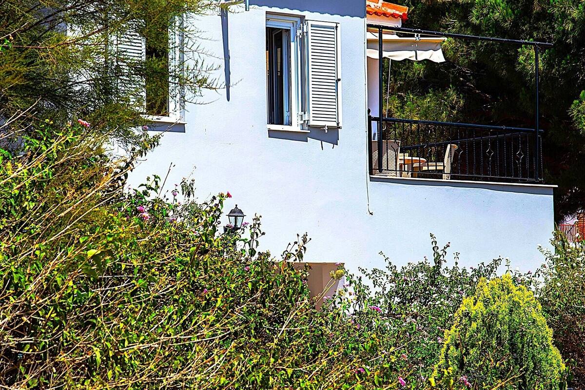Ein weißes Gebäude mit rotem Ziegeldach, einem Balkon mit Geländer und einem kleinen Fenster mit Rollläden.